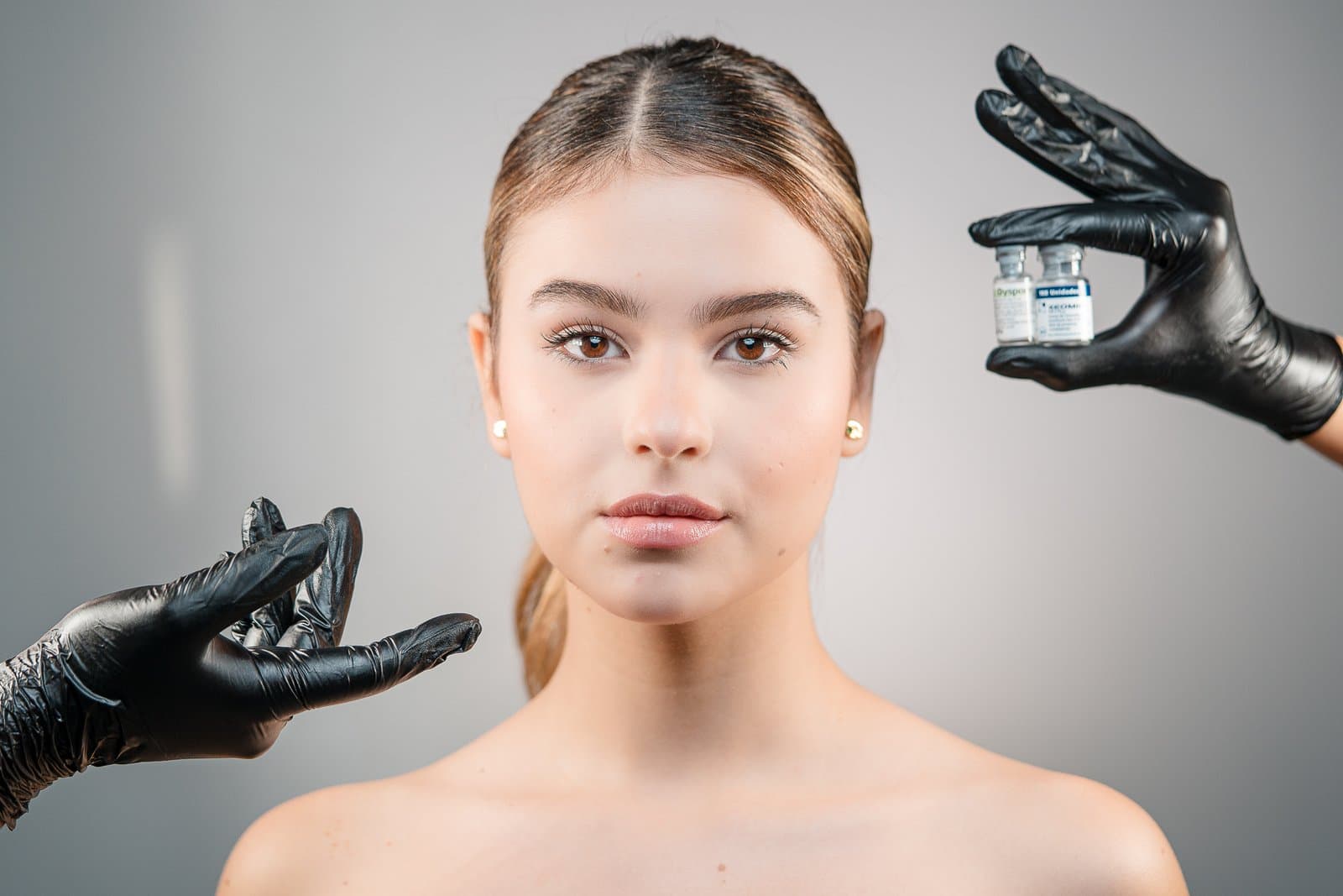 Patient in front of two vials of botulinum toxin held by hands in black gloves